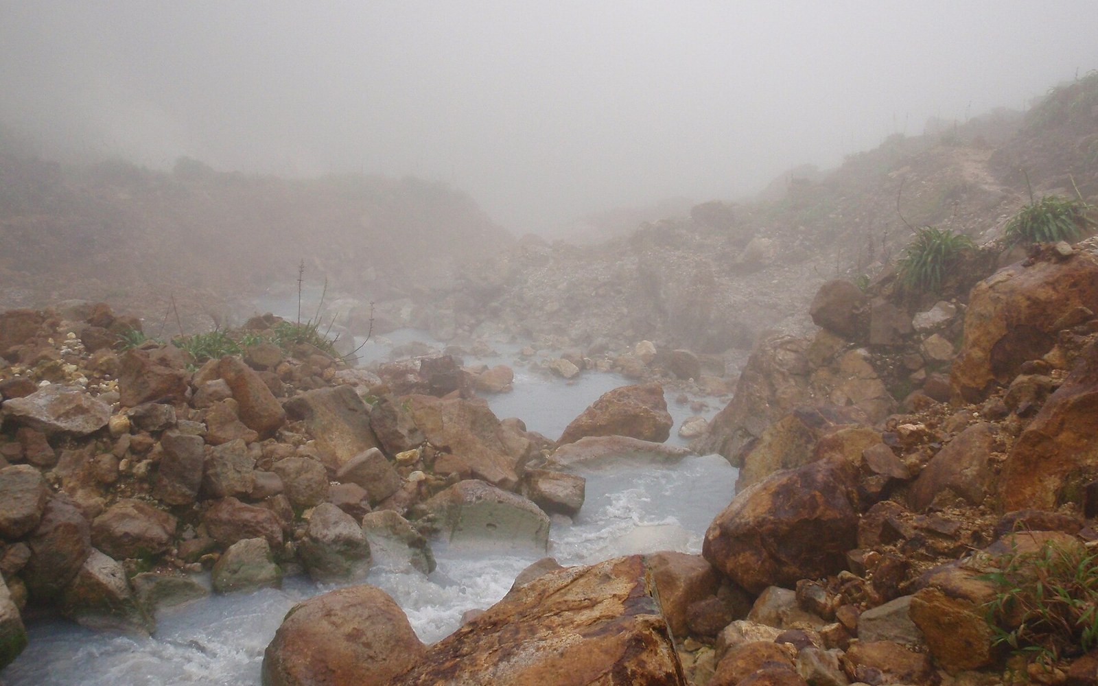 Steam rises over a rocky stream of milky mineral water in a geothermal valley
