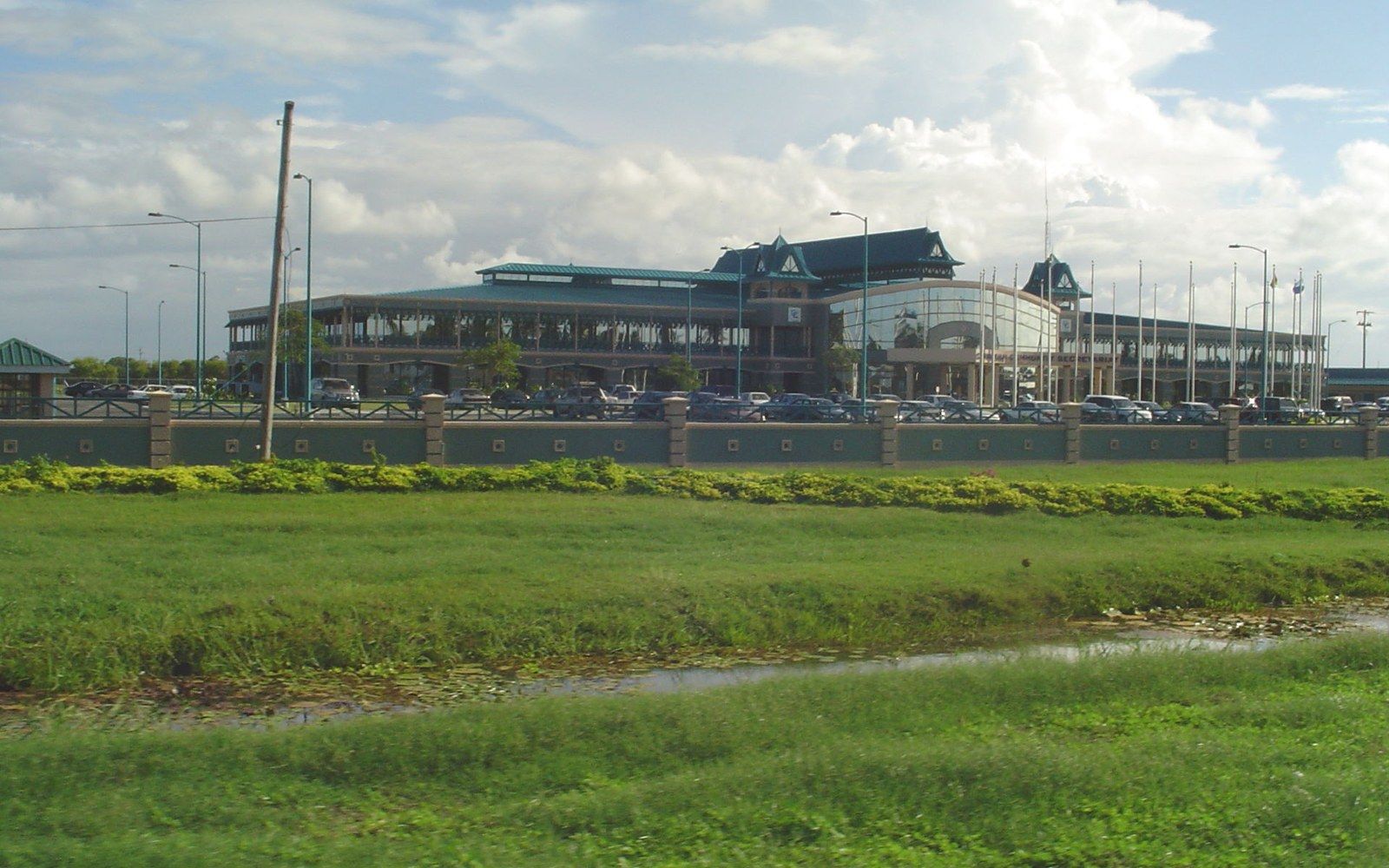 Airport terminal building with parked cars behind a low wall and grassy field
