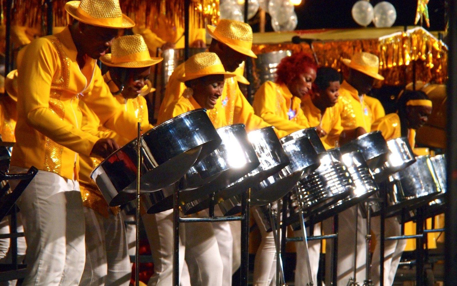 Steel pan musicians in yellow shirts and straw hats perform together on stage at night