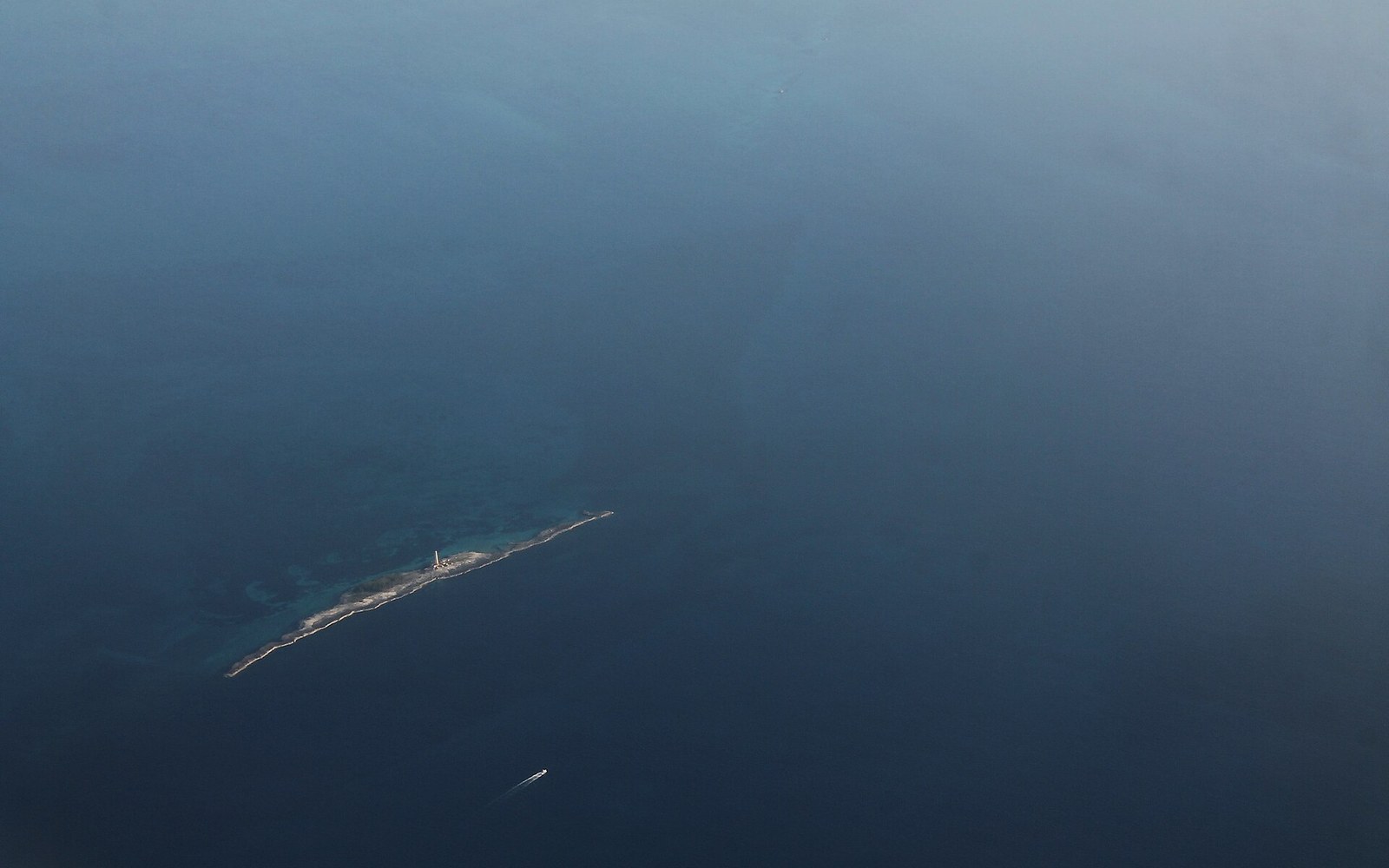 Aerial view of a narrow sandy island with a lighthouse surrounded by open sea