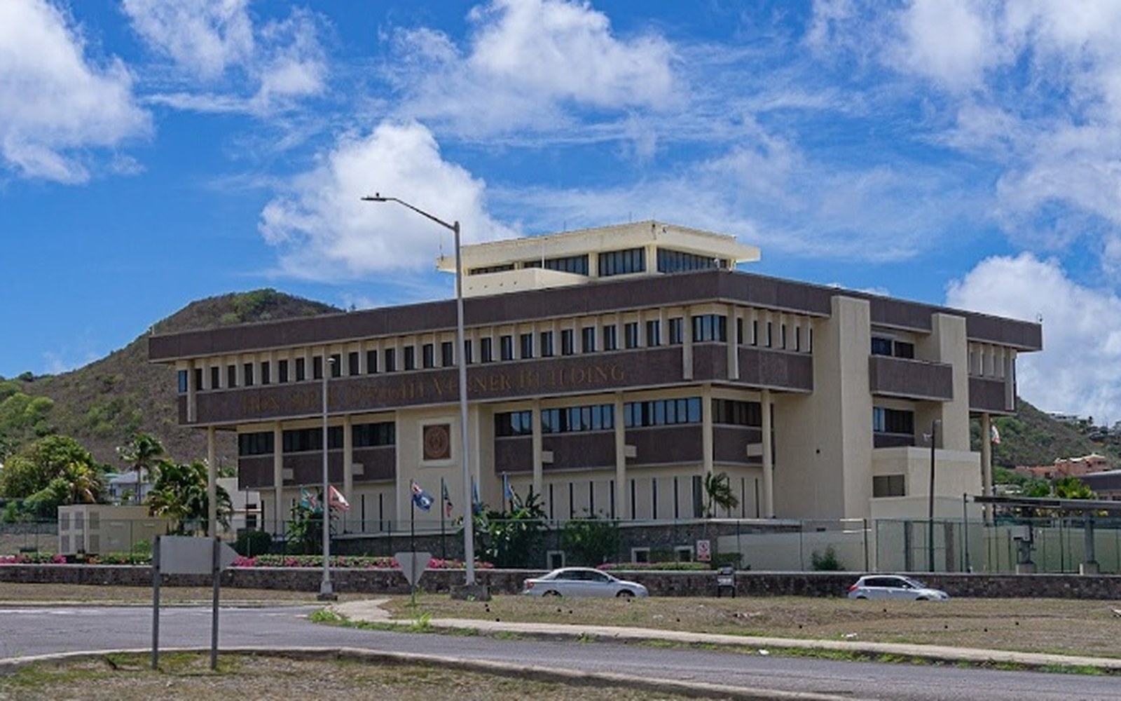 Multistory government building with tiered facade sits below a green hillside