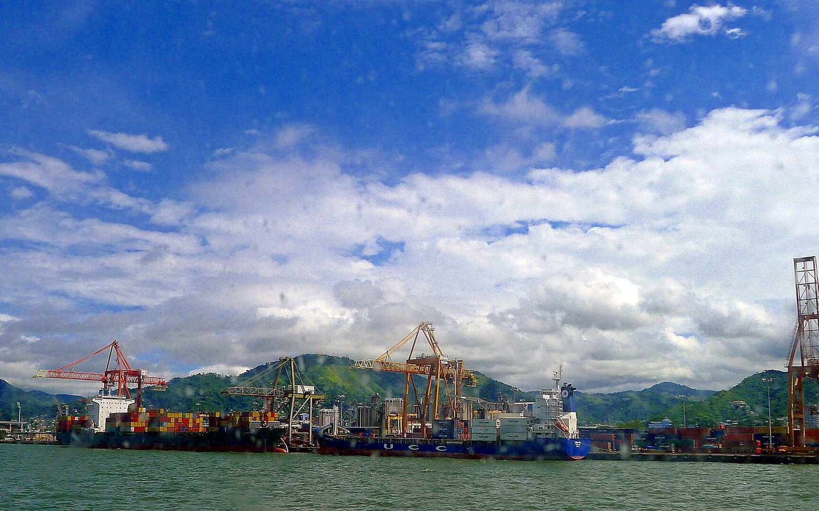 Container ship docked beside gantry cranes at a port with hills in the background