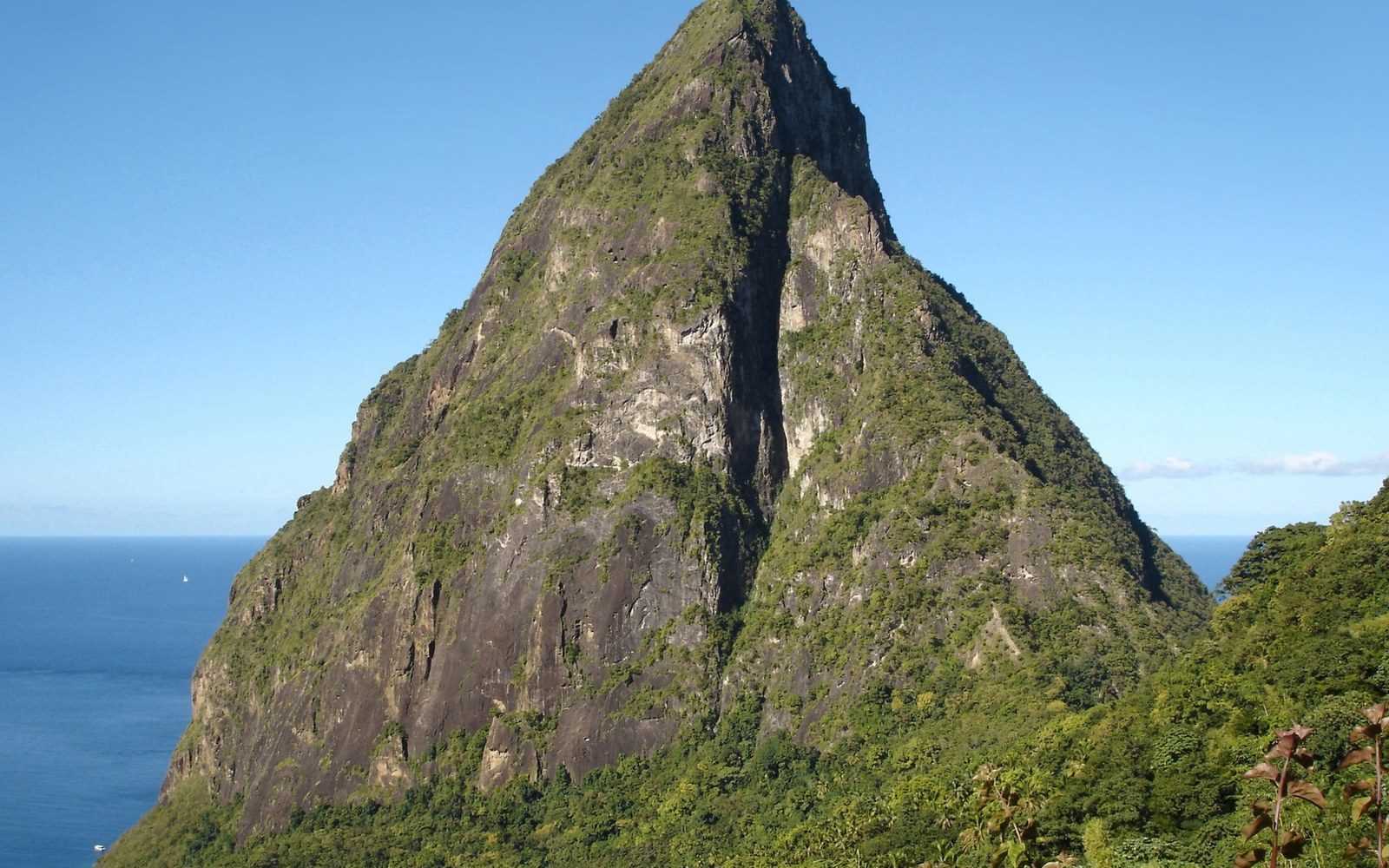 A steep, forested volcanic peak rises sharply above the blue Caribbean Sea
